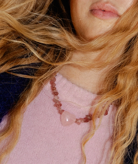 Nika trägt einen rosafarbenen Strickpullover und eine Kette aus kleinen Edelsteinen und einem großen Herzanhänger in Rosa; Zu Schmuck und Accessoires Damen gehen