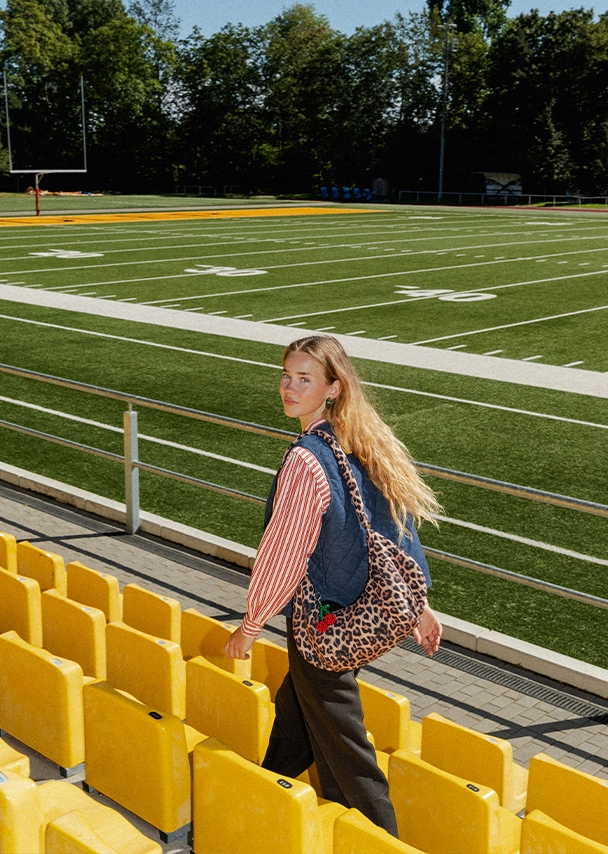 Nika trägt einen gestreiften Sweater in Cremeweiß und Bordeauxrot und darüber eine beigefarbene Fleece-Weste; Zu Jacken Damen gehen