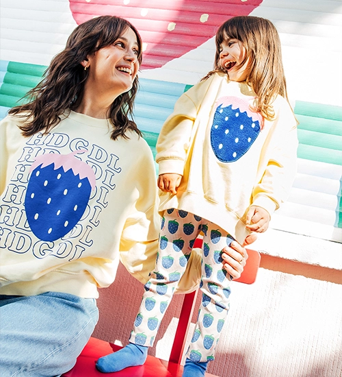 Frau und Kind sind auf einer Bank. Beide tragen einen Sweater mit Erdbeer-Print; Zu KDG x JK gehen