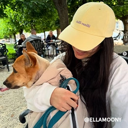 Ella sitzt in einem Park mit einem Hund auf ihrem Schoß. Sie trägt eine Hellgelbe Cap mit lilafarbenen ?CHILLI VANILLI?-Schriftzug; Zur abgebildeten Cap gehen