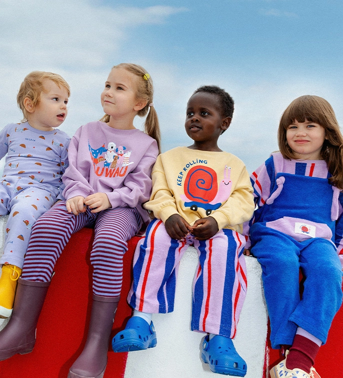 Vier Kinder sitzen auf einer rot-weißen Wand; Zur Keep Rolling Kollektion gehen