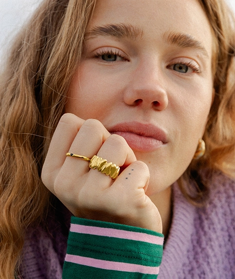 Unser Model Nika ist im Close-up zu sehen. Sie stützt sich auf ihre Hand und man kann gute ihre 2 goldenen Ringe und Ohrringe erkennen. Zu unserer Schmuck-Kollektion.